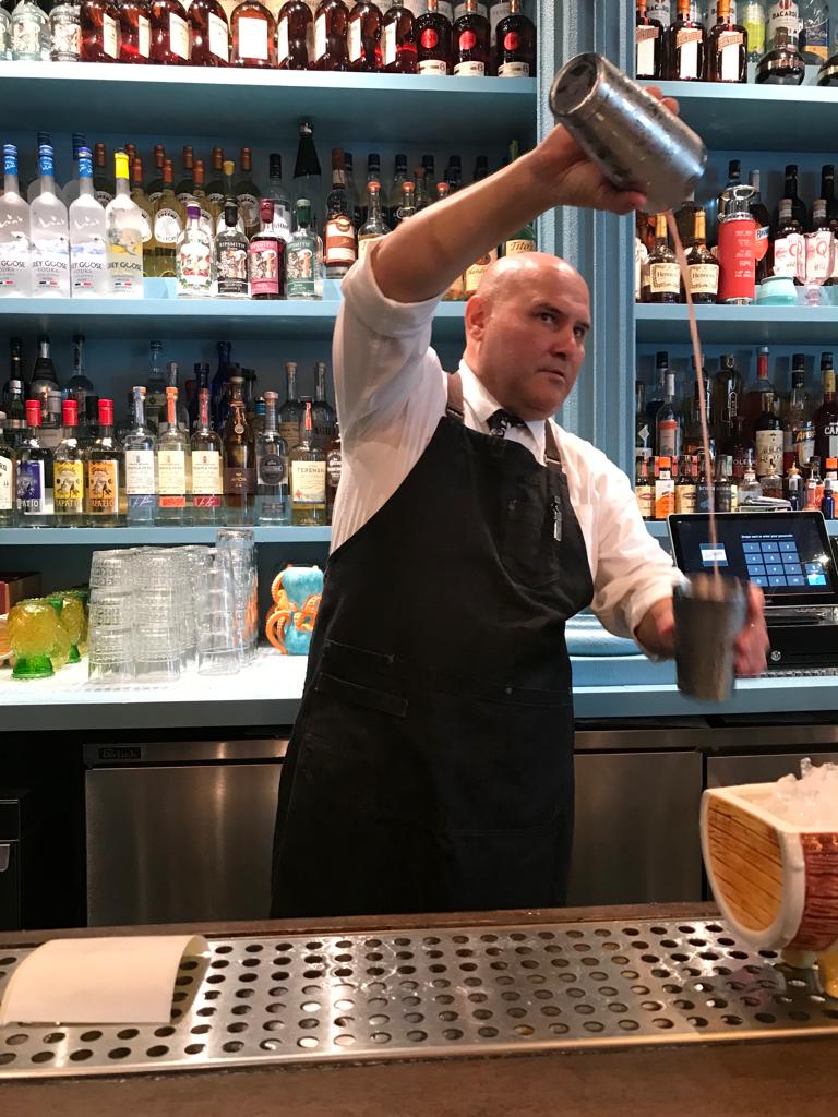 A bartender is pouring a drink into a shaker at a bar.