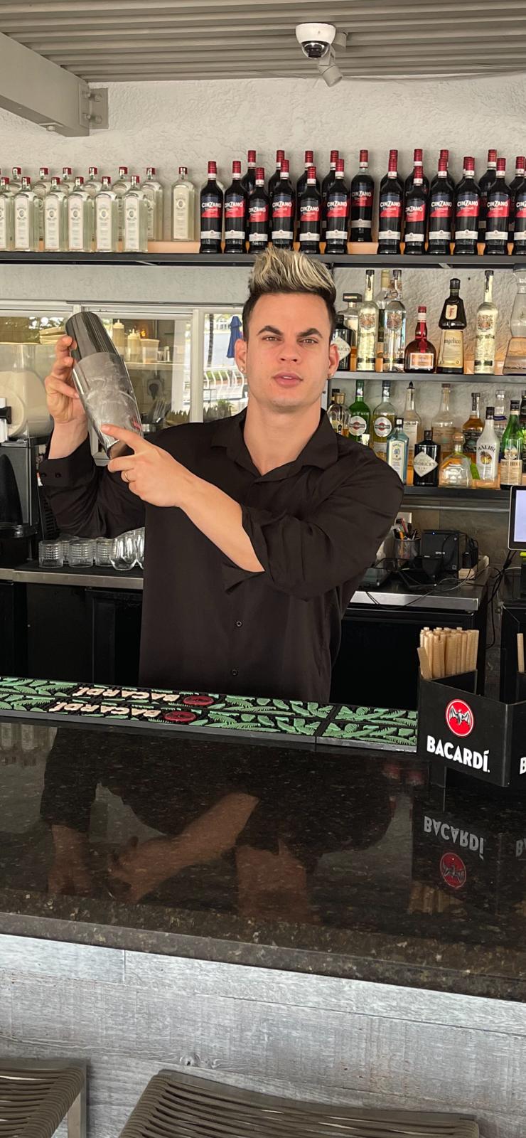 A man is standing behind a bar holding a shaker.