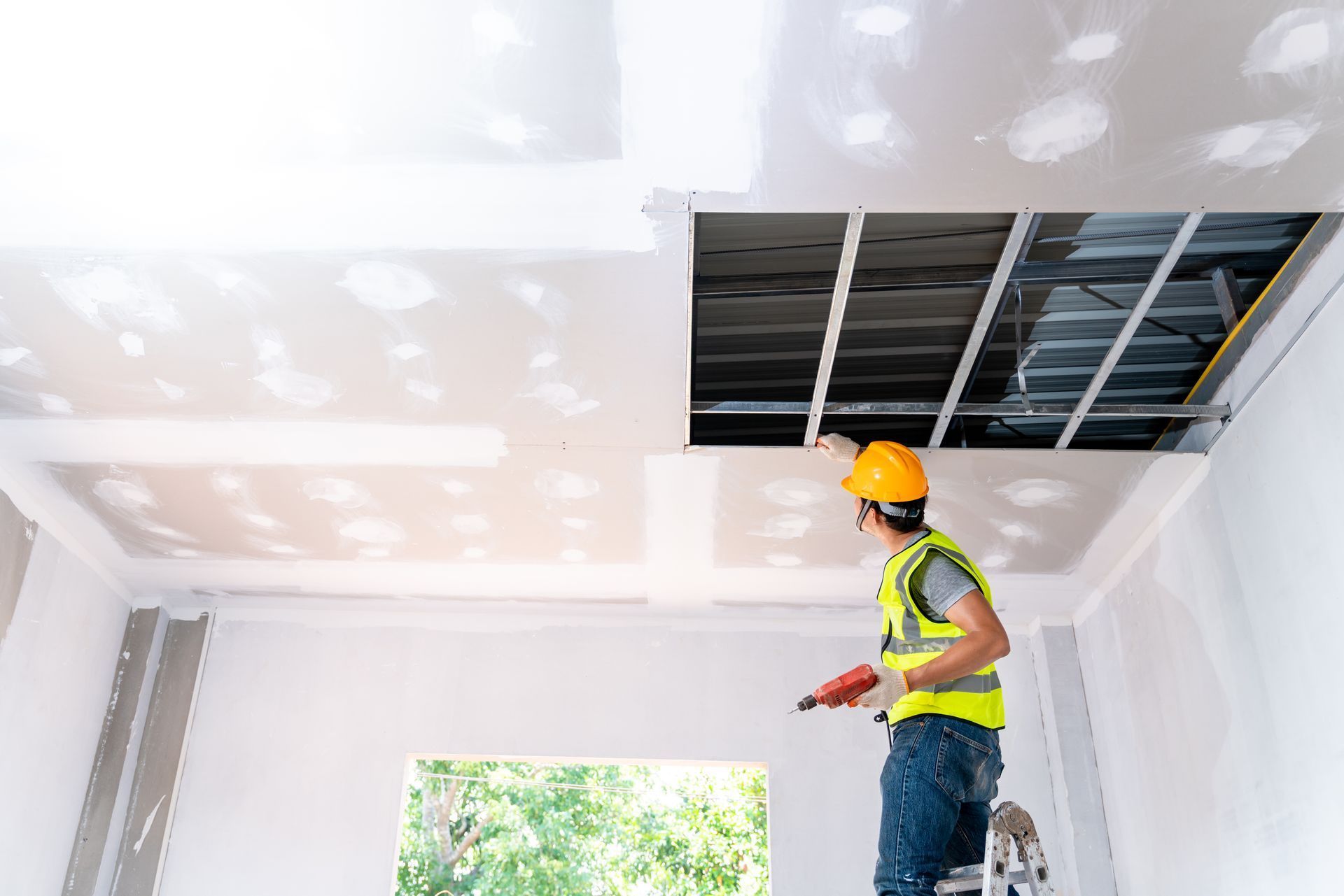 Worker in hard hat repairing a ceiling drywall opening in a bright room