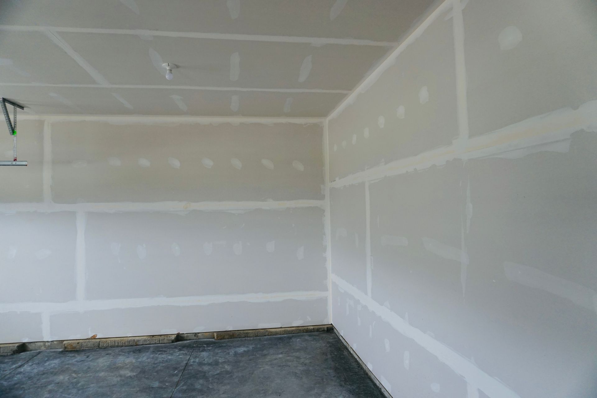 Empty drywall garage interior with white walls, unfinished floor, and ceiling seams visible