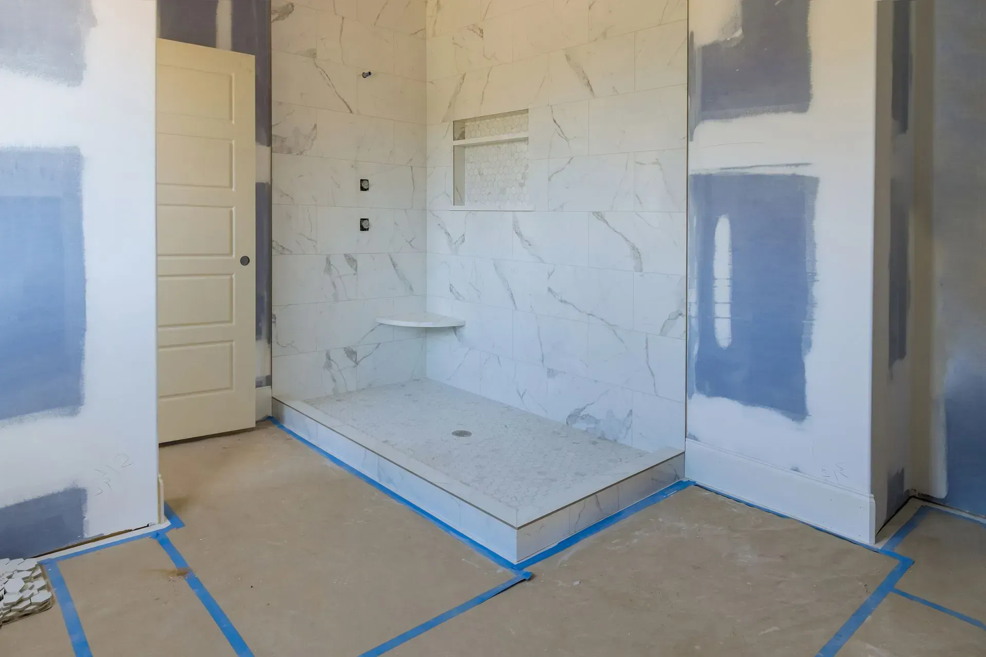 Unfinished bathroom with tiled shower nook, blue drywall patches, and taped floor protection