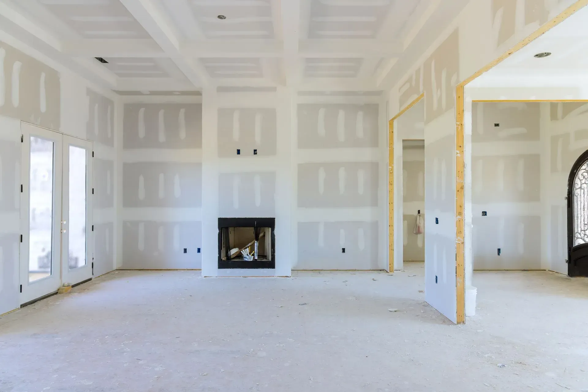 Empty unfinished living room with drywall, a fireplace, and large windows.