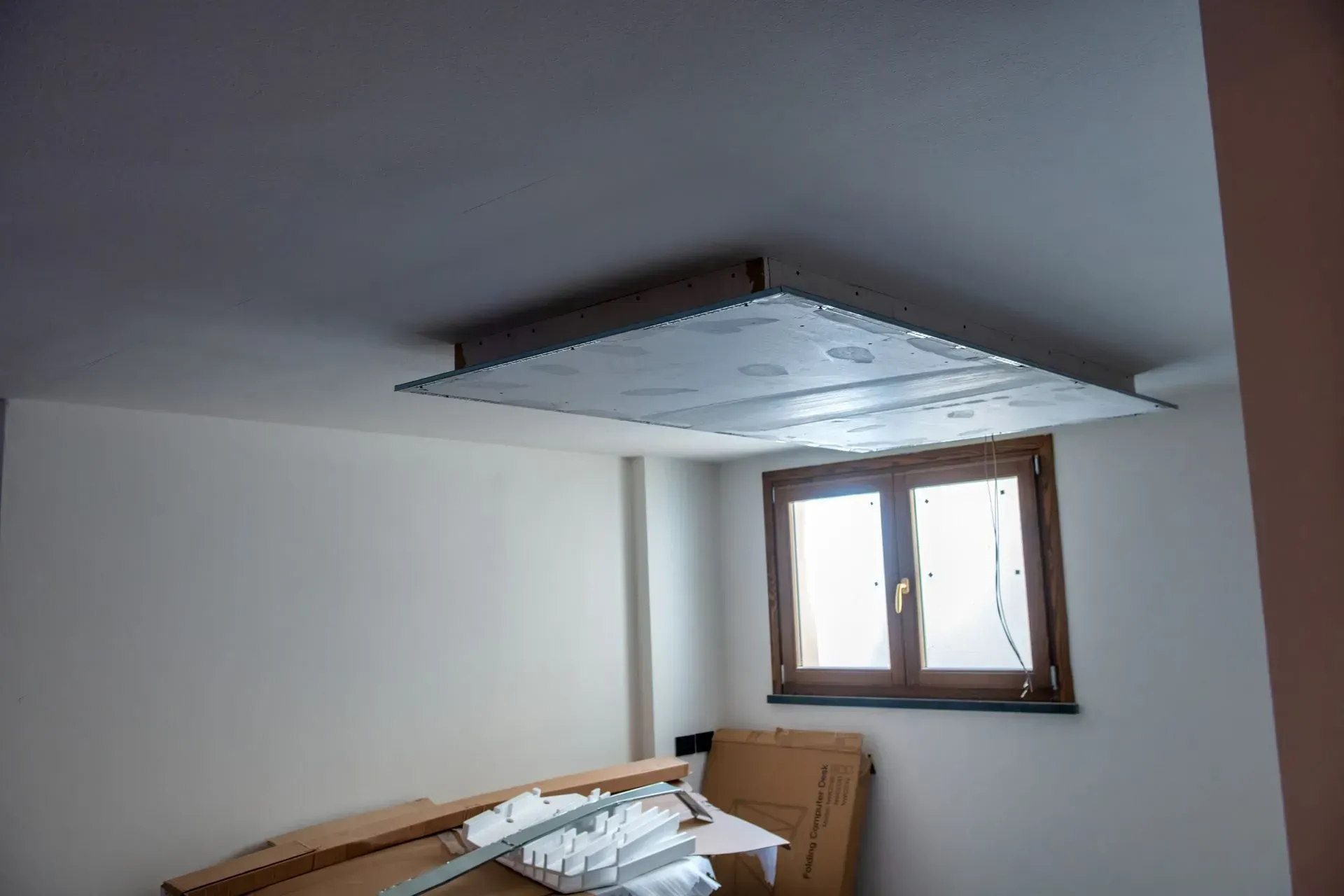 Unfinished room with exposed ceiling panel and a window above stacked building materials.