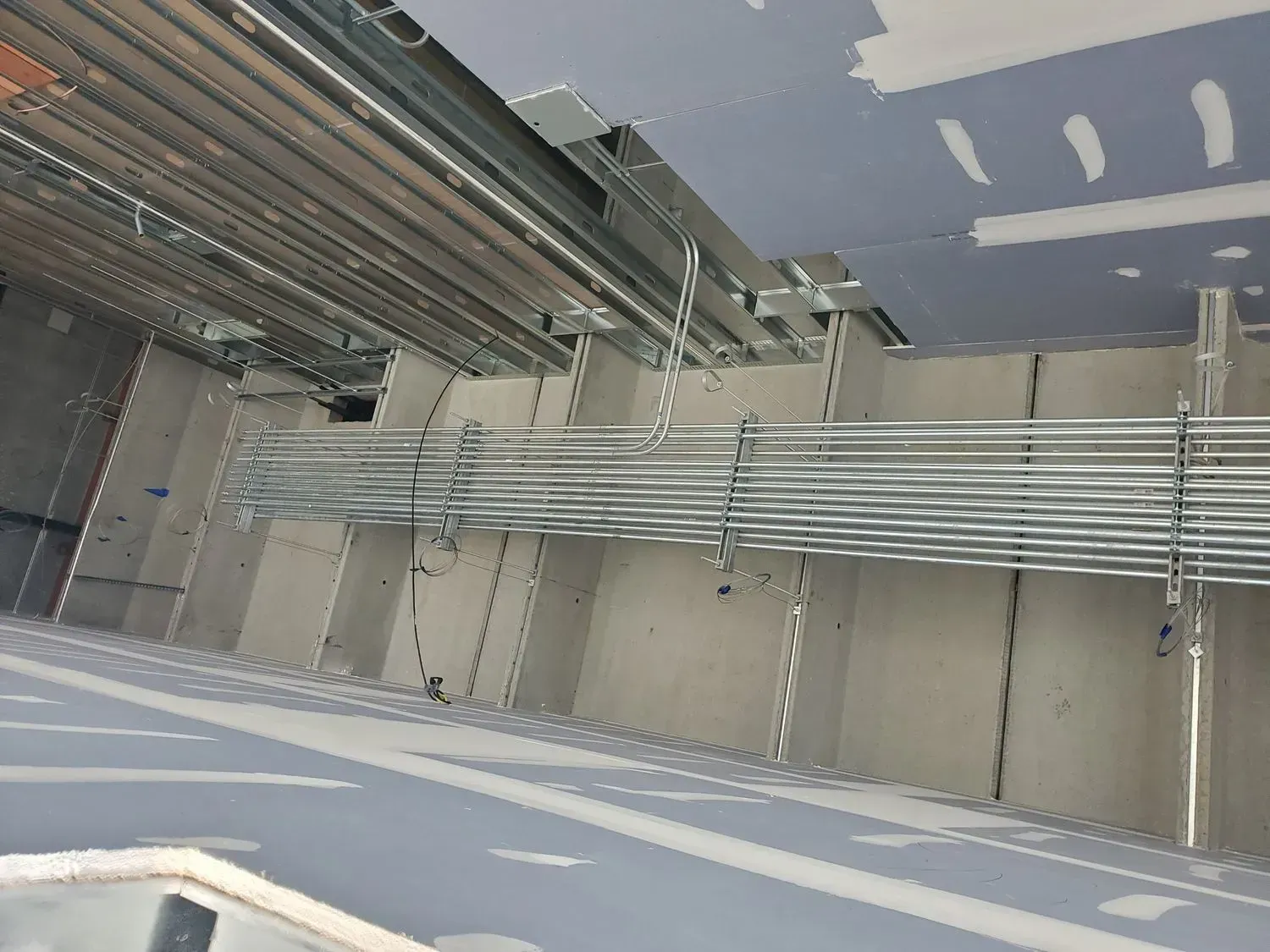 Industrial ceiling with bundled metal conduits and cable trays in a gray utility room