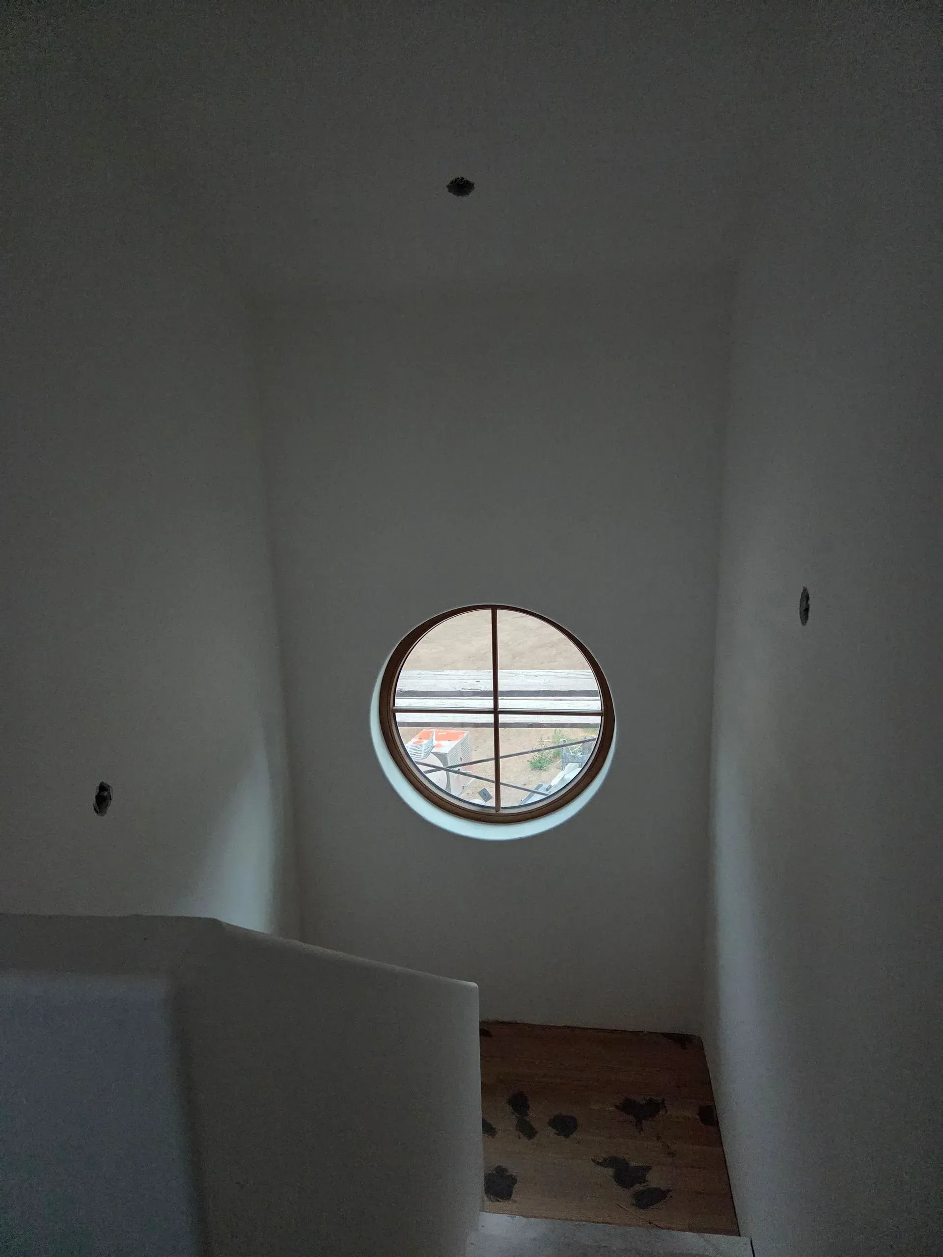 Narrow stairwell with white walls and a round window at the far end.