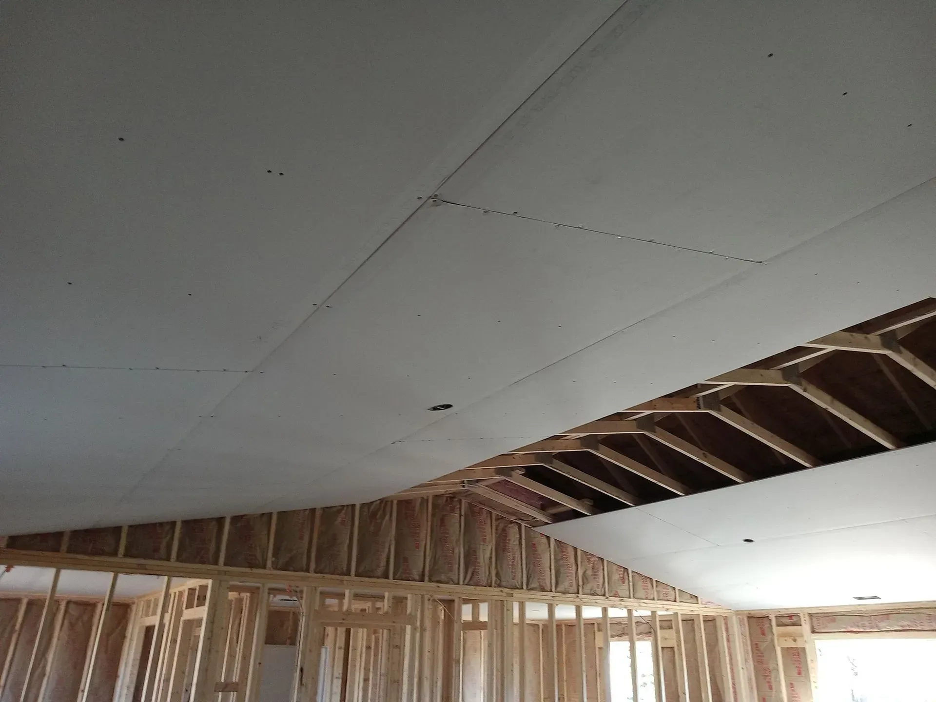 Partially finished room with exposed wood framing and a white ceiling panel being installed