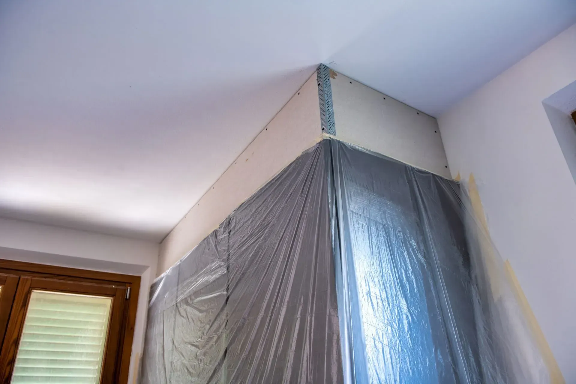 Room corner wrapped in plastic sheeting, with a window and ceiling visible.