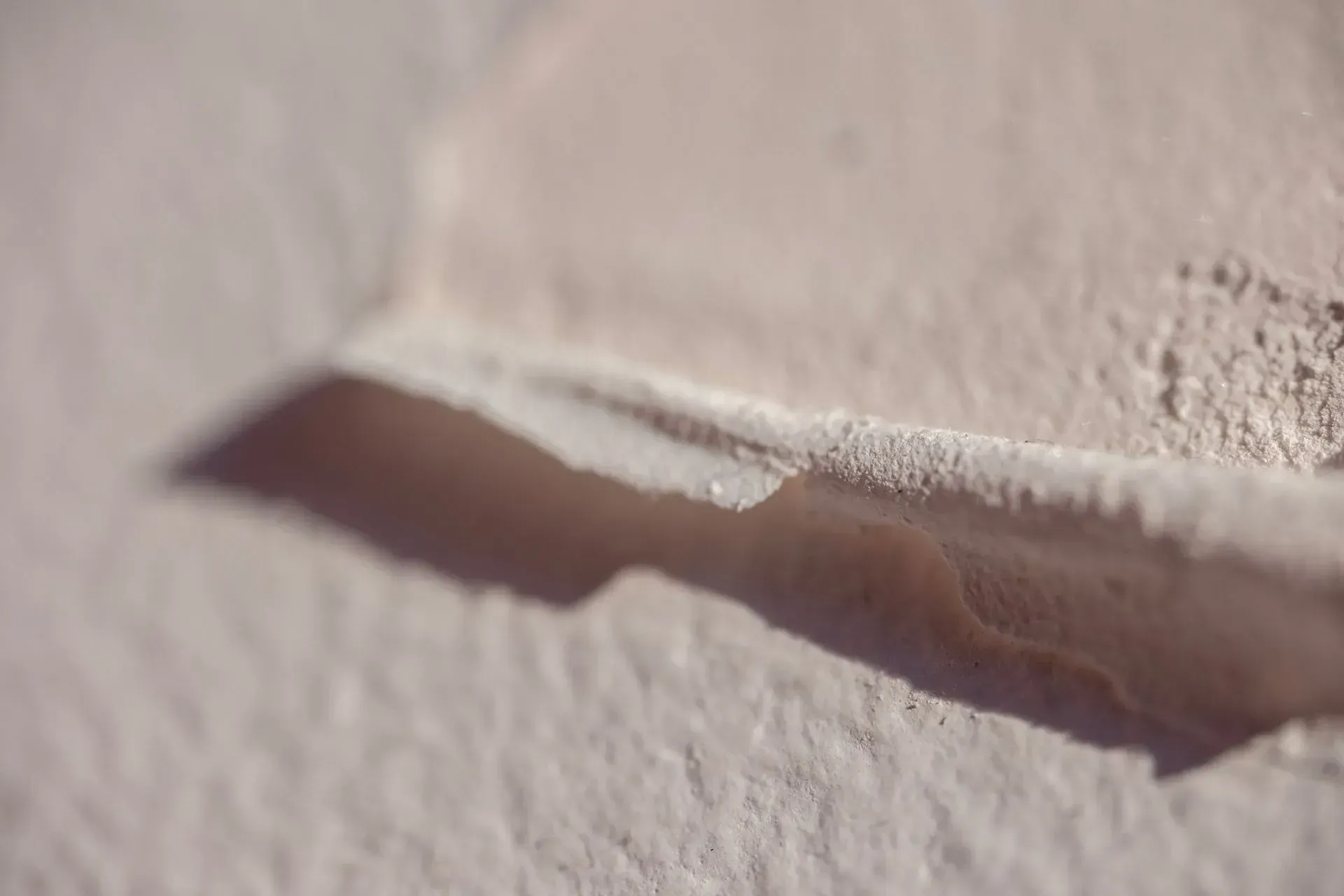 Close-up of a white textured surface with a torn or peeling edge exposing a shadowed crease