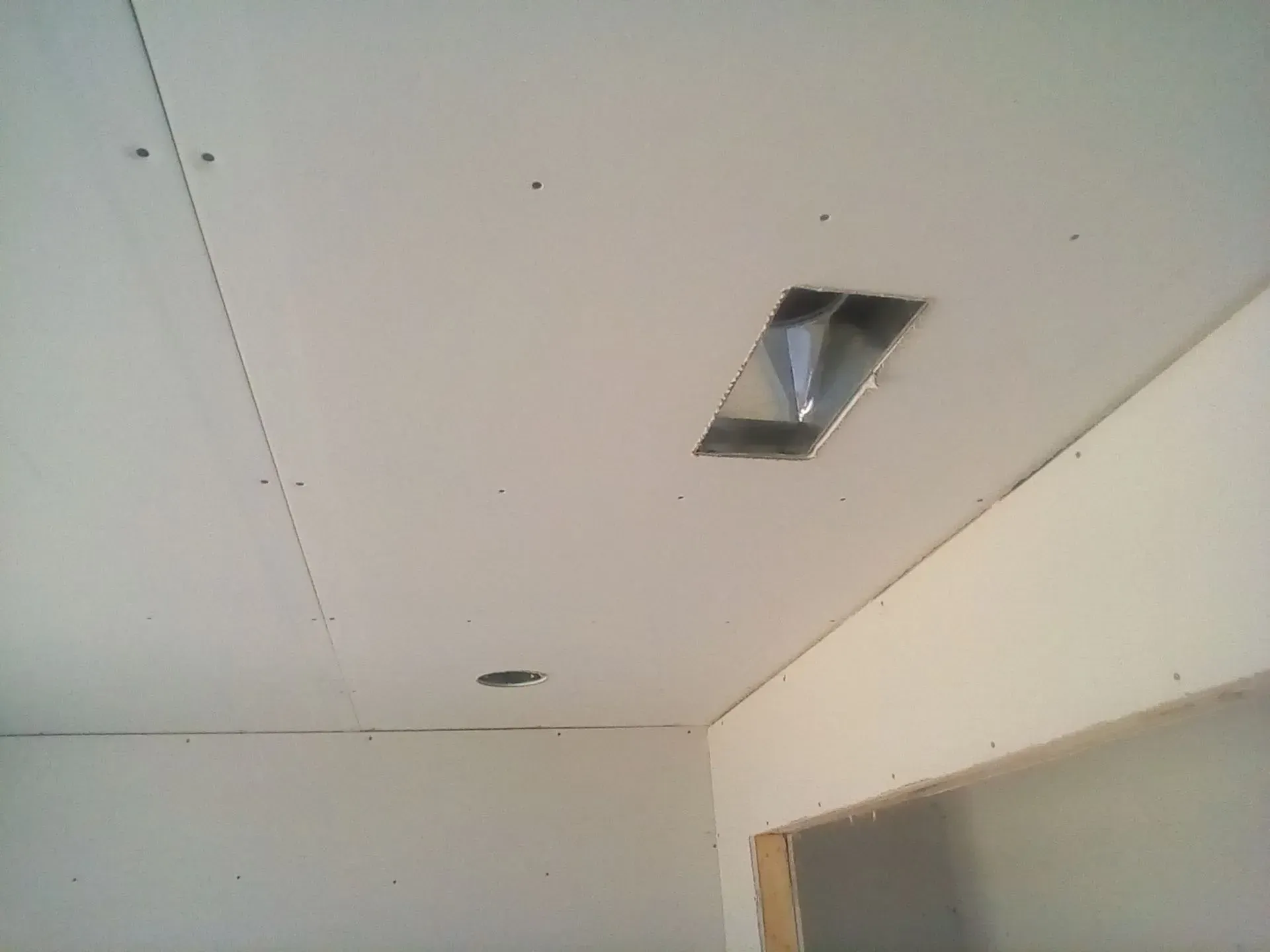 White ceiling with recessed light opening and small holes in a corner of a room