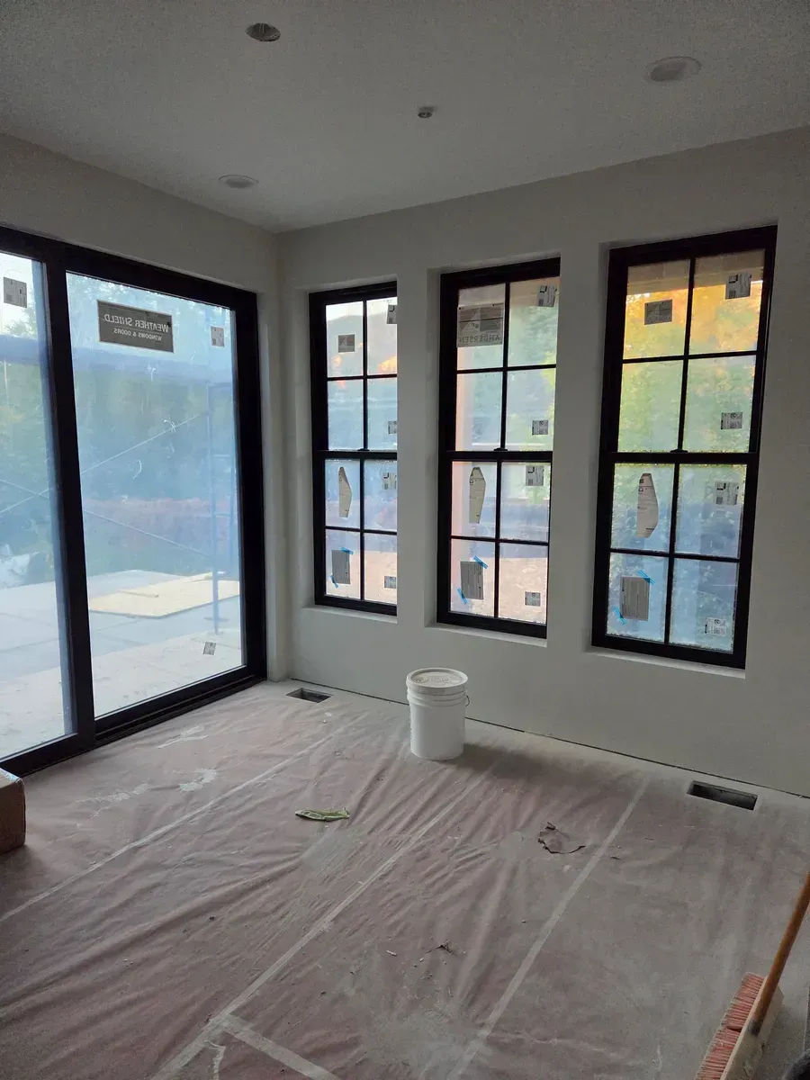 Empty room with black-trimmed windows and covered floor, lit by daylight.