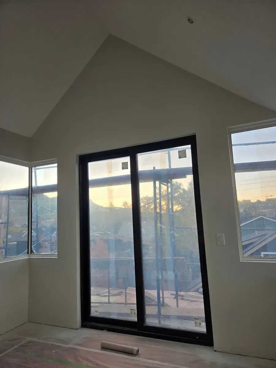 Empty room with vaulted ceiling, black-framed glass doors, and two windows overlooking sunset outside