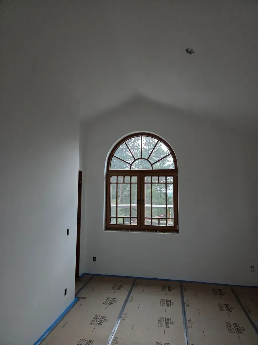 Empty white room with arched window, tiled floor, and blue painter’s tape along the baseboards