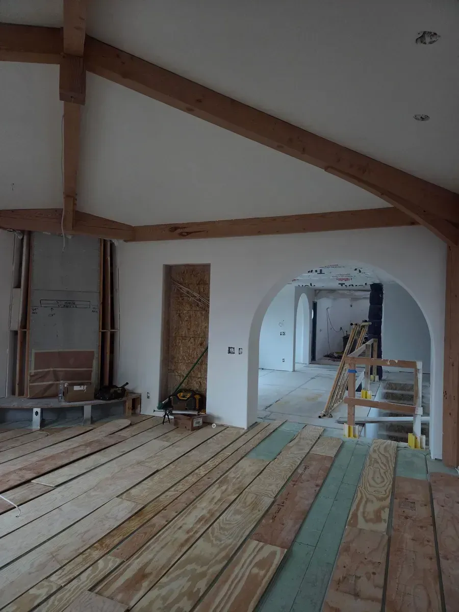 Renovated room with exposed wood beams and unfinished plank flooring, viewed through an arched doorway