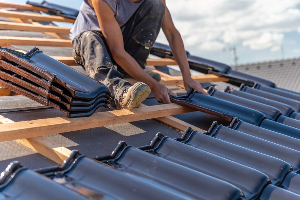 Roofer installing dark gray roof tiles on wooden frame roof.