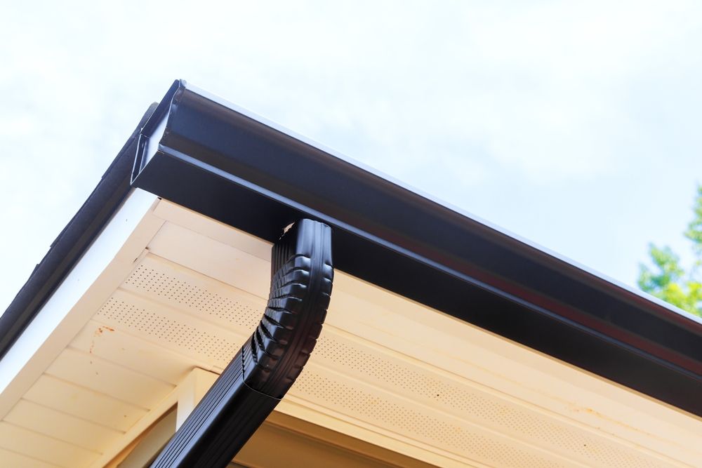 Black gutters and trim on a house with light beige siding against a cloudy sky.