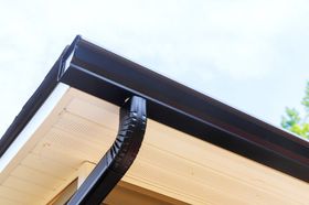 Black gutters and trim on a house with light beige siding against a cloudy sky.