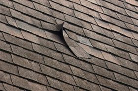 Close-up of a brown asphalt shingle roof with a damaged shingle.