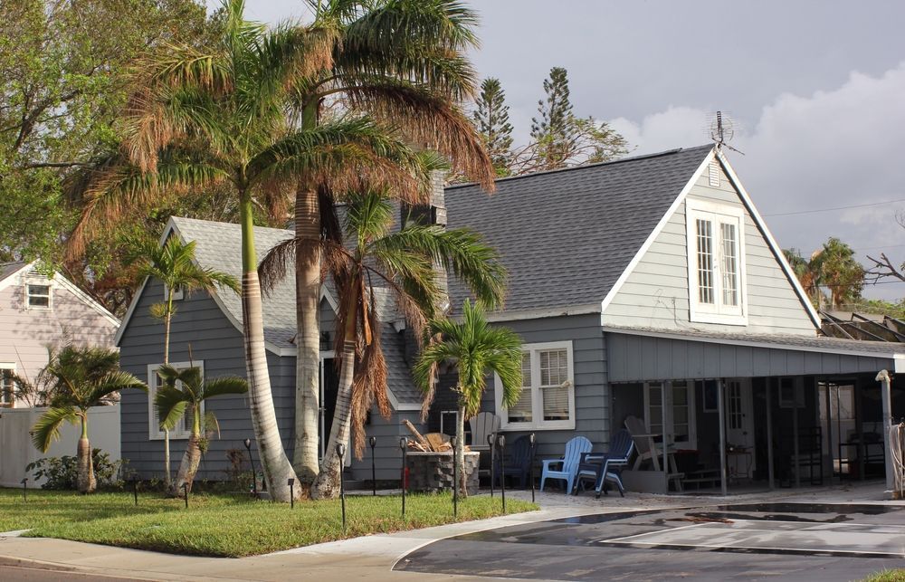 Blue house with gray roof, palm trees in front, screened porch, blue chairs.