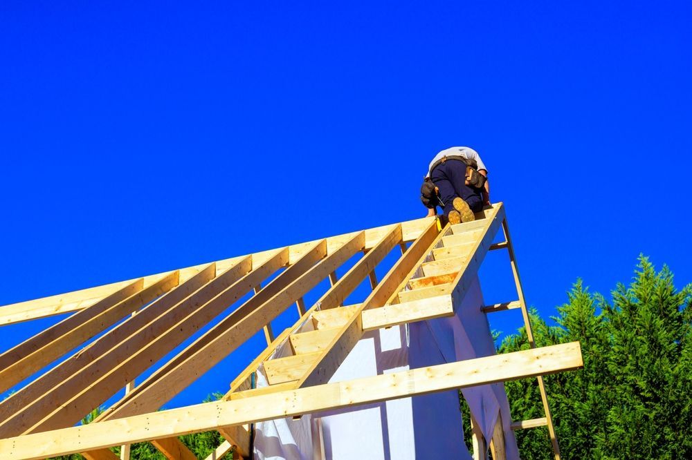 Construction worker on a rooftop framework under bright blue sky.