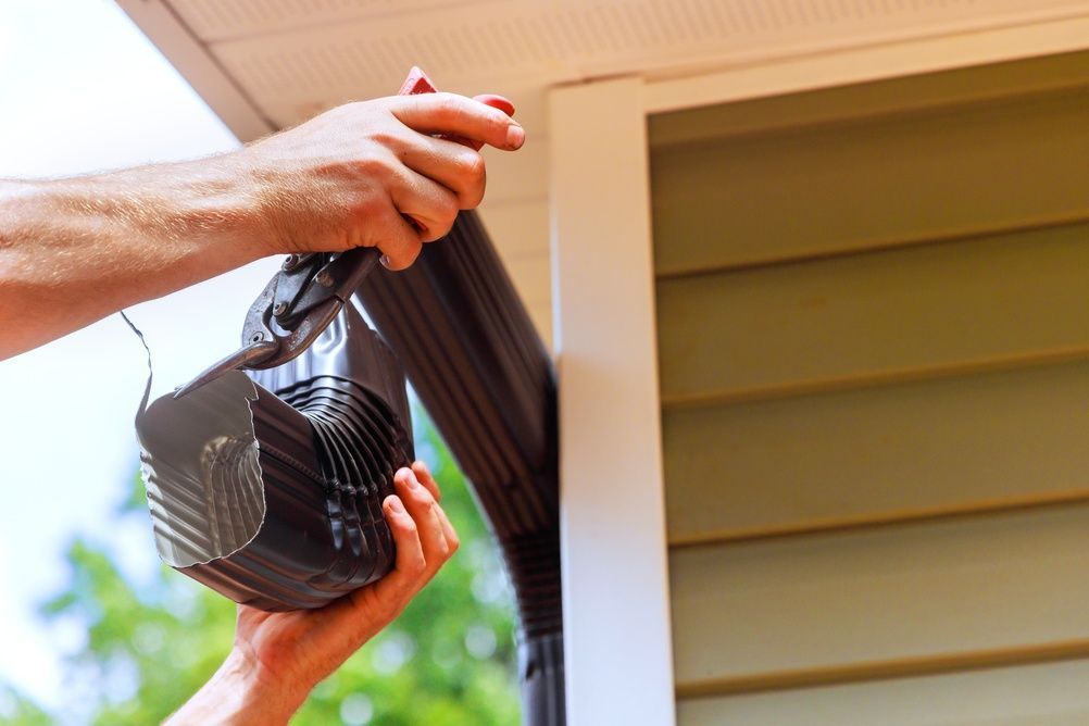 Person installing a brown gutter on a house, close-up view.