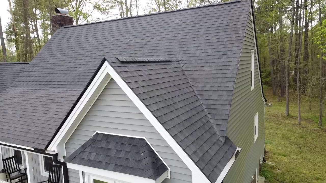 House with gray roof and siding, white trim, set in a wooded area.