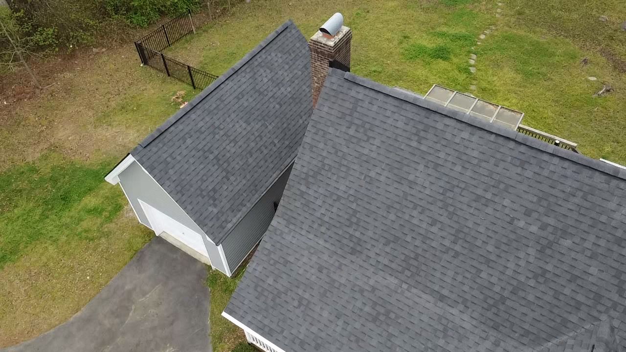 Overhead view of two buildings with dark gray roofs, green grass, and a chimney.