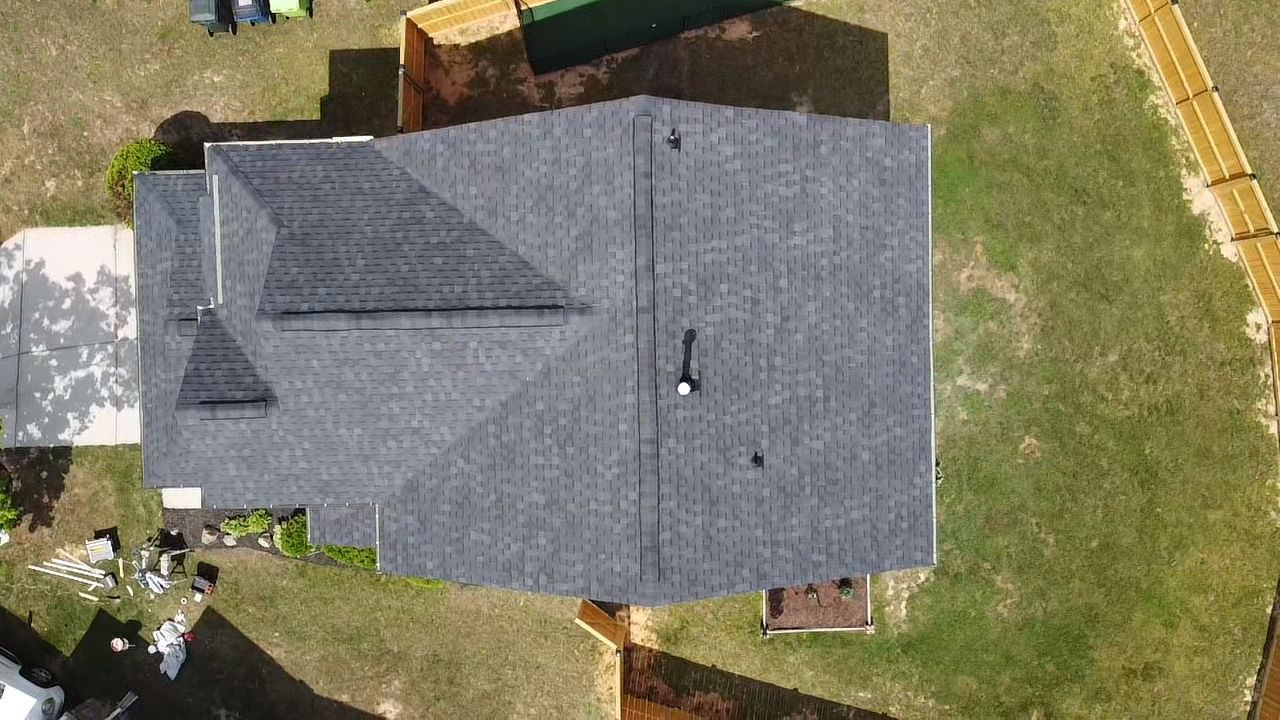 Overhead view of a house with a dark gray roof, surrounded by grass and a wooden fence.