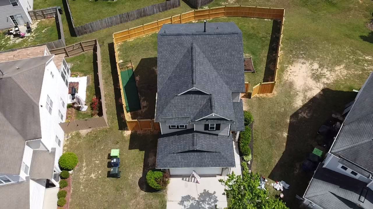 Overhead view of a gray house with a dark roof, fenced backyard, and a driveway.