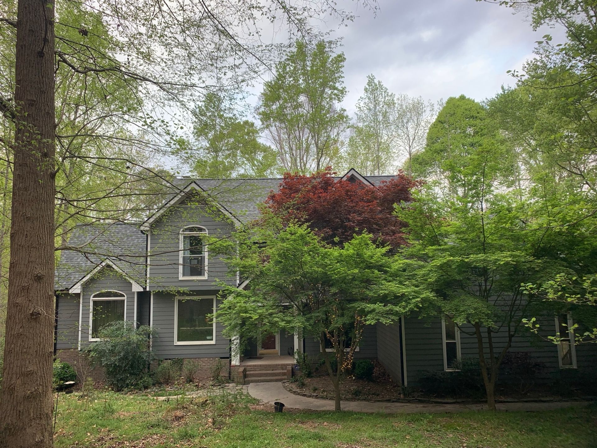 Gray house with gray roof, nestled in trees with red and green leaves.