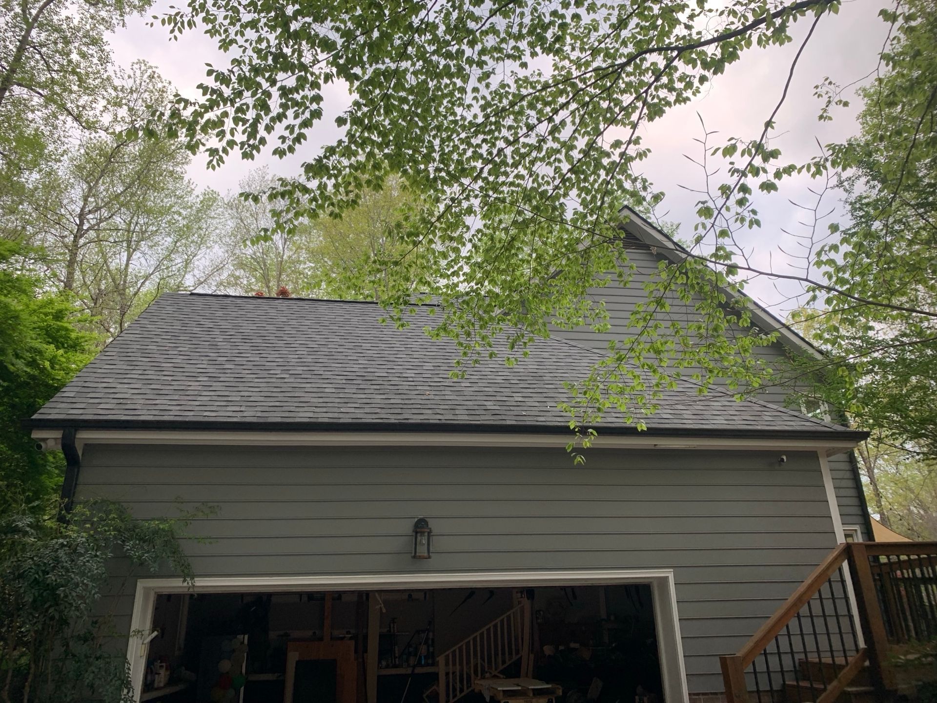 Garage with gray roof and green siding, viewed from below trees against a cloudy sky.