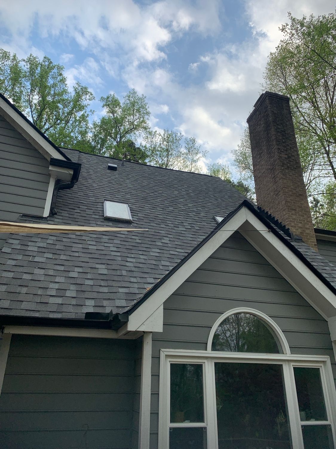 Gray house with gray roof and brick chimney against a cloudy sky.