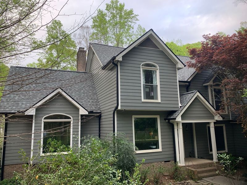 Gray two-story house with gray roof, white trim, and a porch surrounded by trees and greenery.
