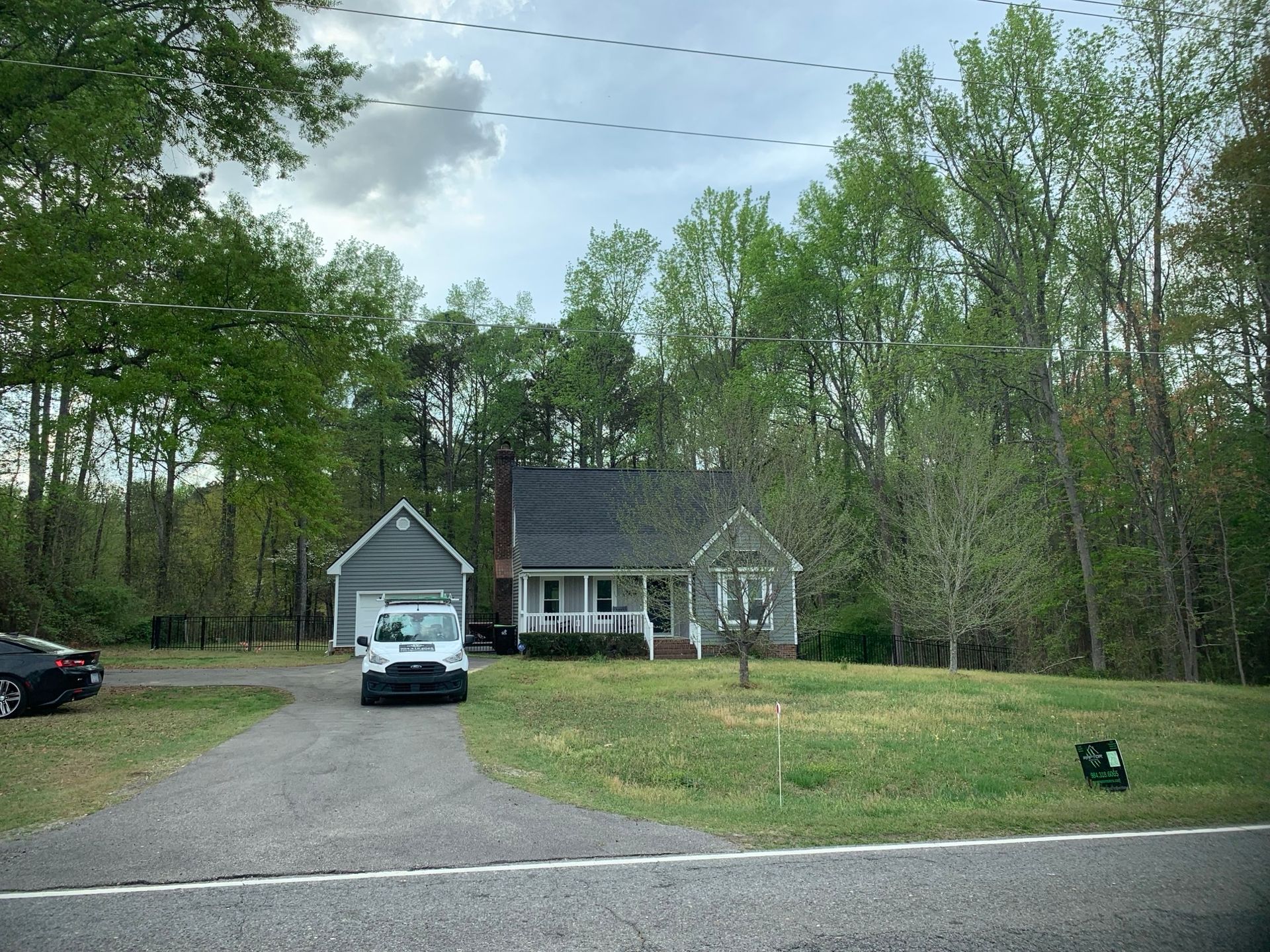 Small house with a gray garage and driveway, a white car, and lush green trees.