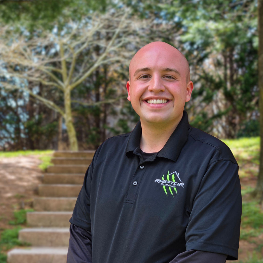 Man in blue polo shirt smiles outdoors near stairs.