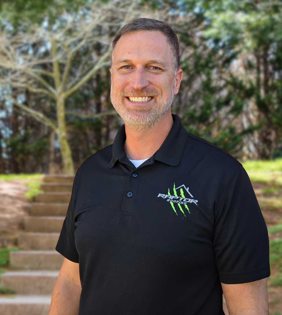 Man in black polo shirt smiles outdoors near stairs.