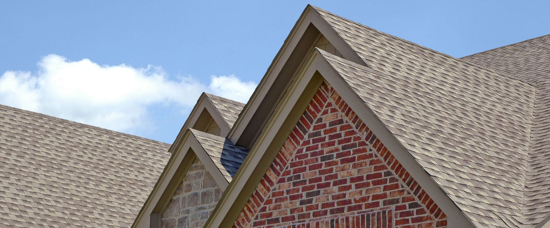 A brick house with a tan roof and a blue sky in the background.