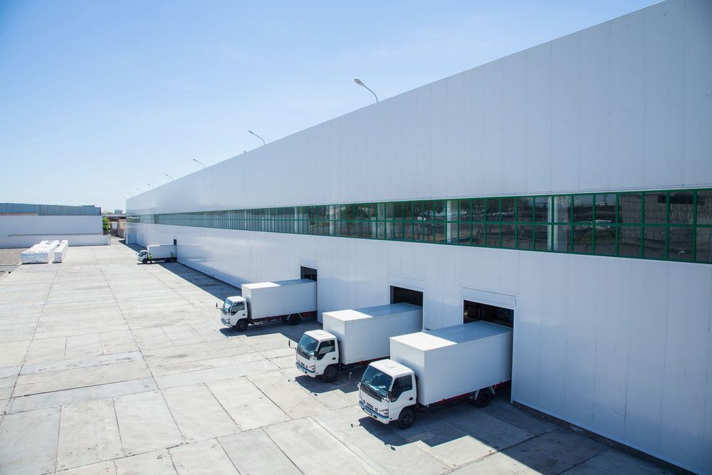 White Trucks Backed Into Loading Docks of a Large, White Warehouse — Curtis Strata in Yamba, NSW