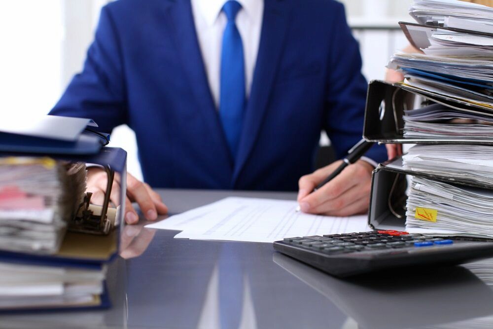Man in Blue Suit at Desk, Surrounded by Paperwork and Calculator, Writing — Curtis Strata in Coffs Harbour, NSW
