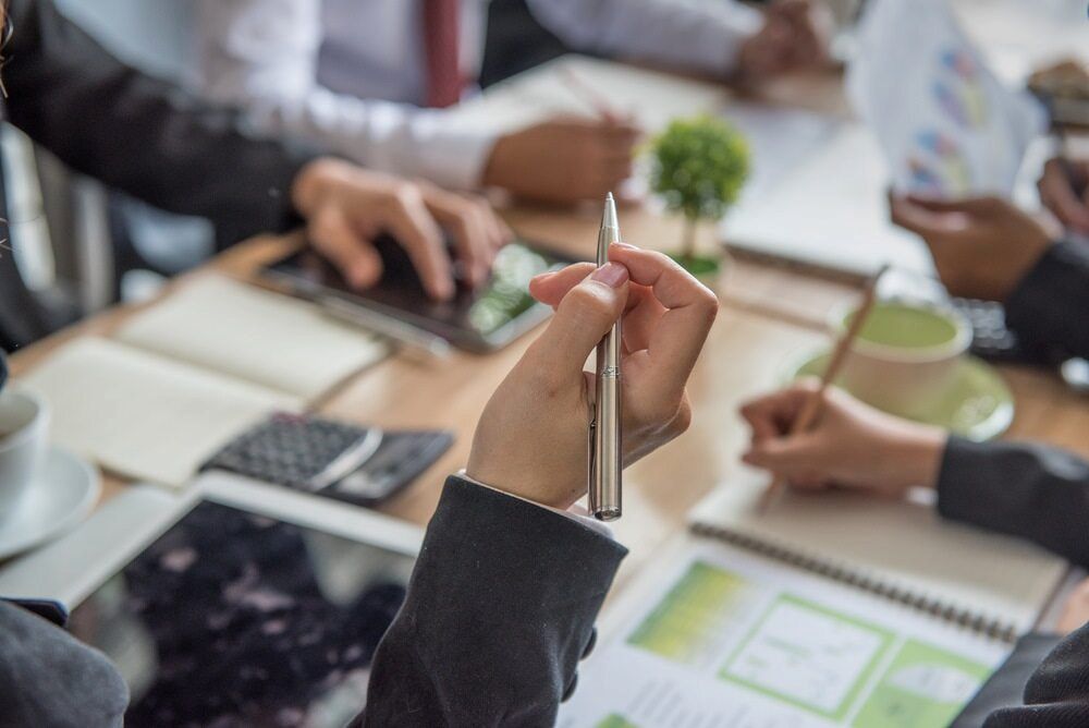 Business Meeting Around a Table, Hands Holding Pens, Laptops, and Documents — Curtis Strata in Murwillumbah, NSW