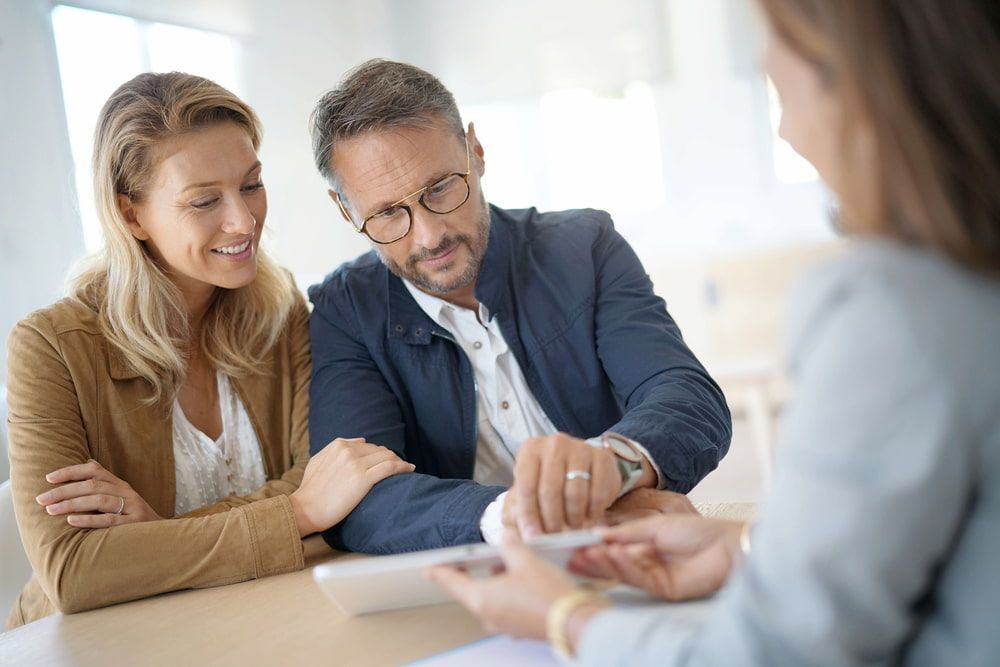 Couple Reviews Document With a Professional, Smiling at a Table in an Office — Curtis Strata in Byron Bay, NSW