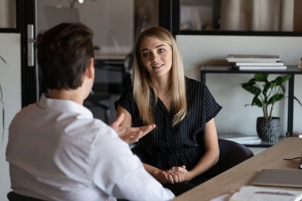 a Woman in a Black Top Smiles, Gesturing Towards a Man at a Desk — Curtis Strata in Woolgoolga, NSW