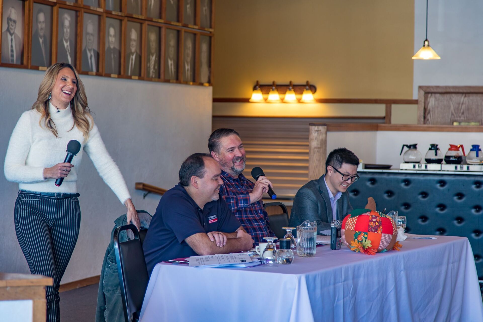 A woman is holding a microphone in front of a group of people sitting at a table.