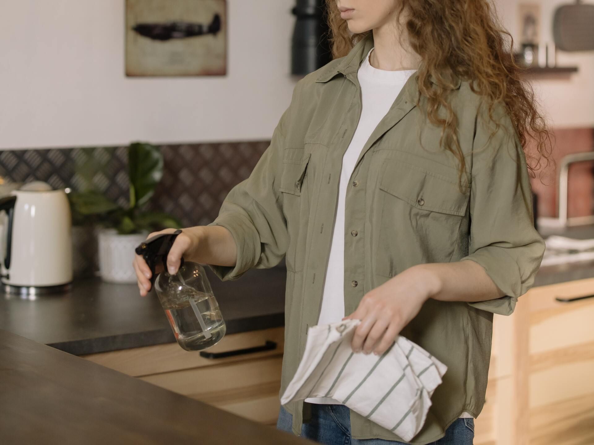 A woman is cleaning a kitchen counter with a spray bottle and a towel.