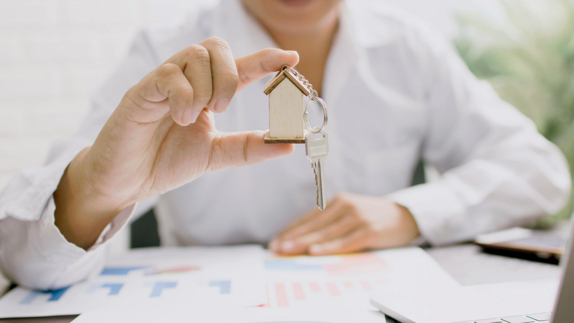 Hand holding a little house keychain over some paperwork.