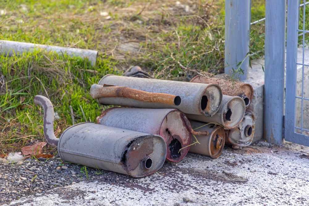 Pile of Rusty Car Mufflers Near a Metal Gate and Green Grass — Independent Scrap Metal Pty Ltd in Ballina, NSW
