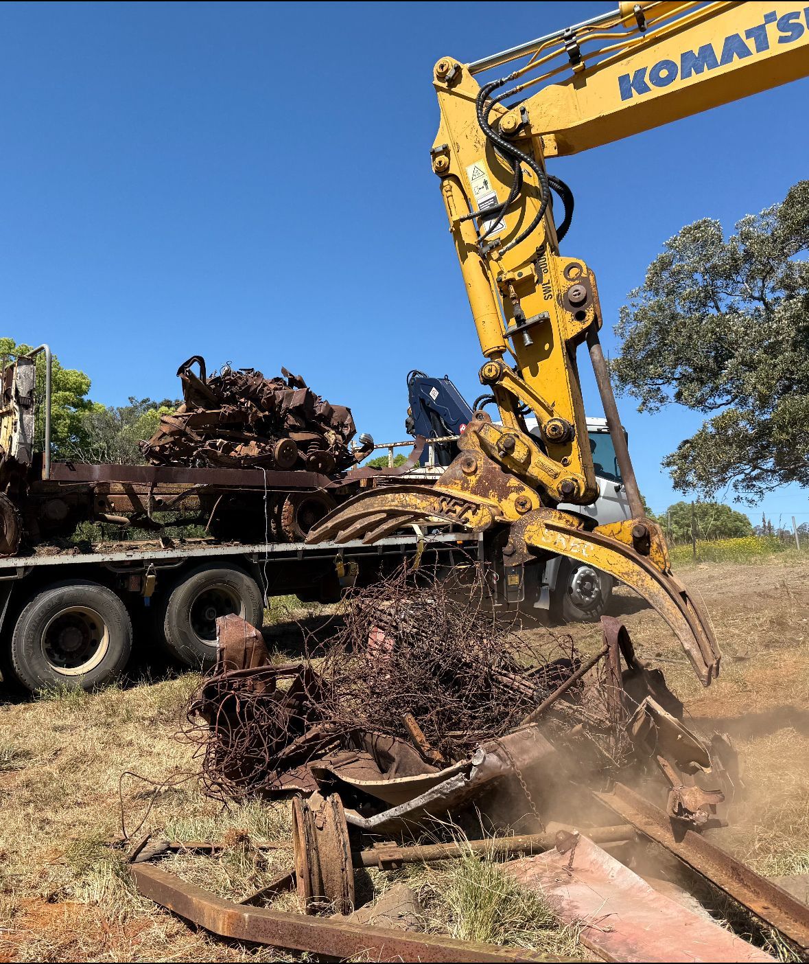 Yellow excavator loading scrap metal onto a flatbed truck on a sunny day— Independent Scrap Metal Pty Ltd in South Lismore, NSW