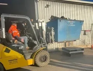 Forklift Operator Lifting a Blue Dumpster in Front of a Warehouse — Independent Scrap Metal Pty Ltd in South Lismore, NSW
