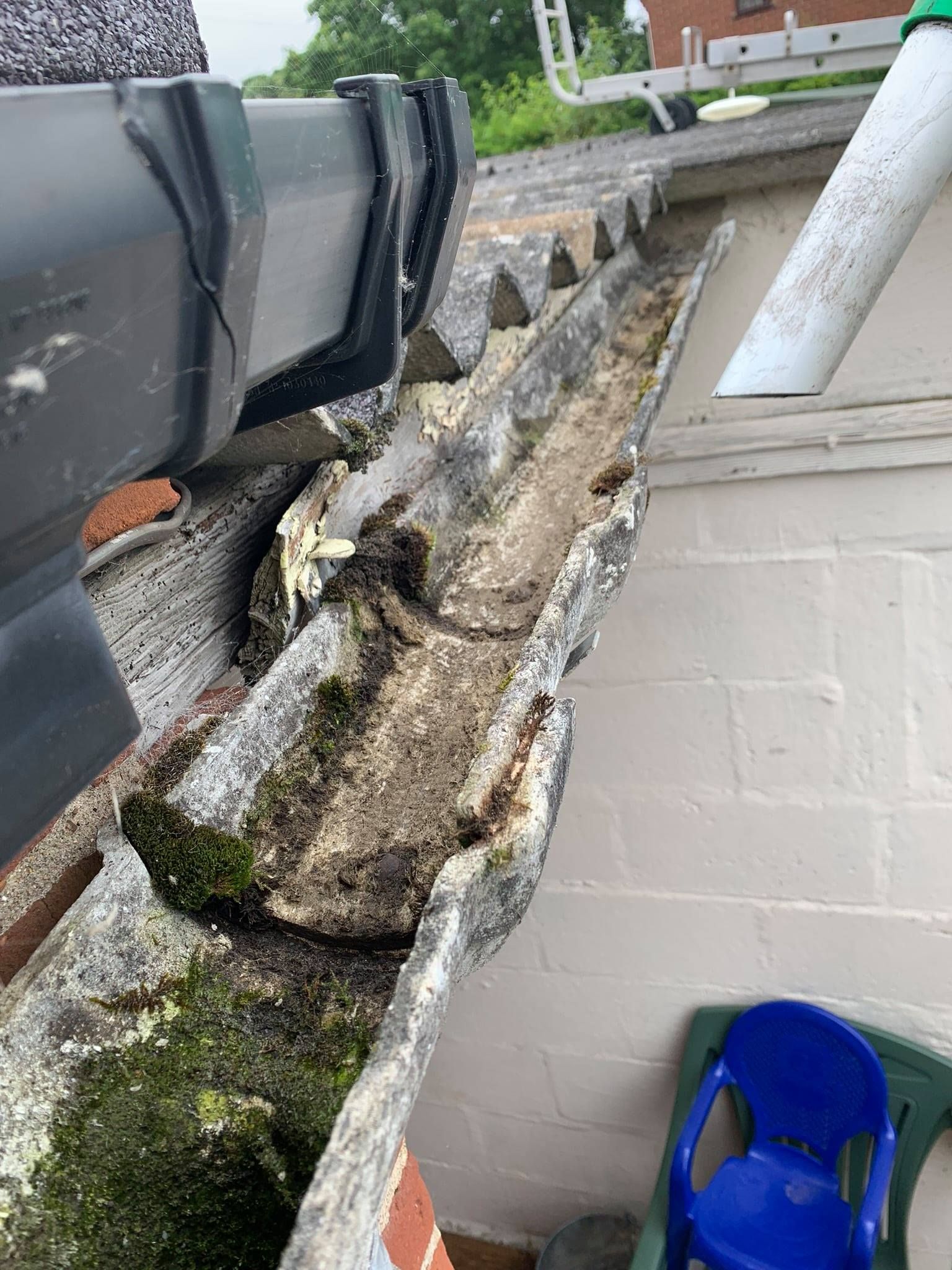 Close-up of the same gutter, now cleared of most moss and debris, next to the drainpipe on the roof, with a cleaner appearance.