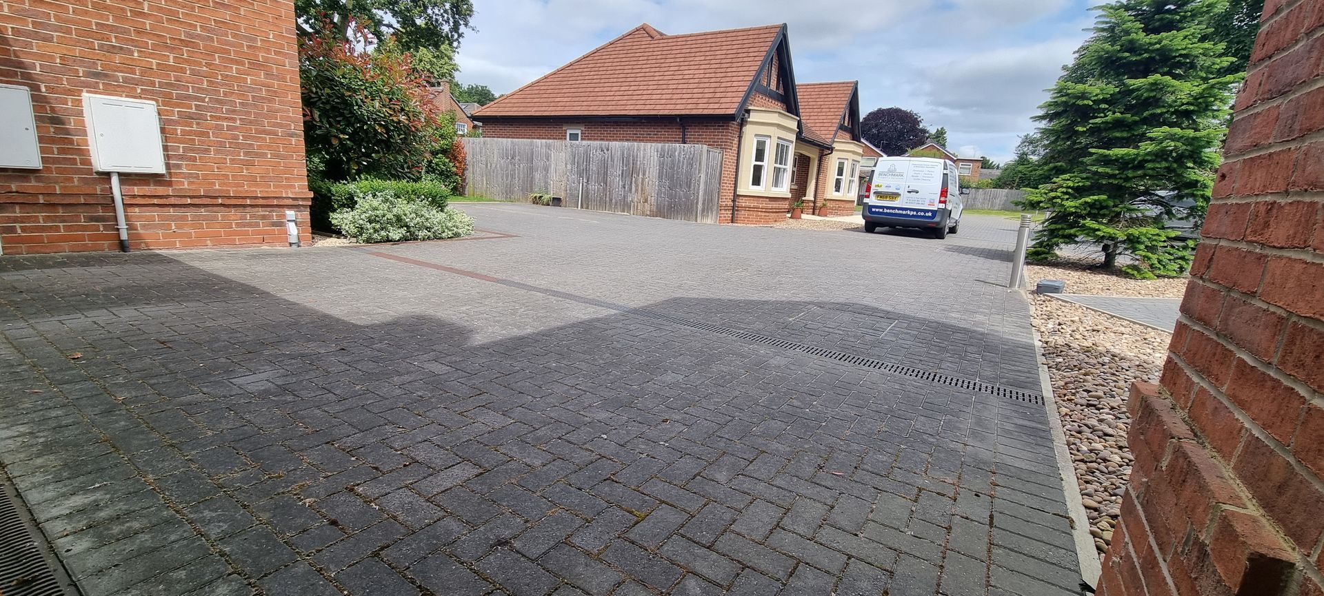 A block paved driveway in front of a brick house after being pressure washed by benchmark property services.