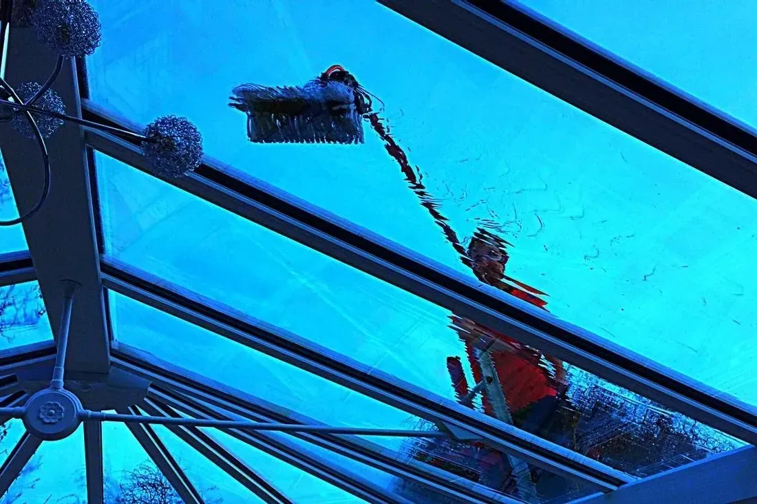 A man is cleaning a glass roof with a water fed pole.